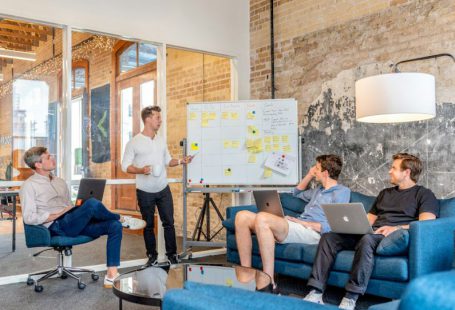 Robo-advisor - three men sitting while using laptops and watching man beside whiteboard