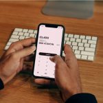 Finance Apps - a man holding a cell phone in front of a keyboard